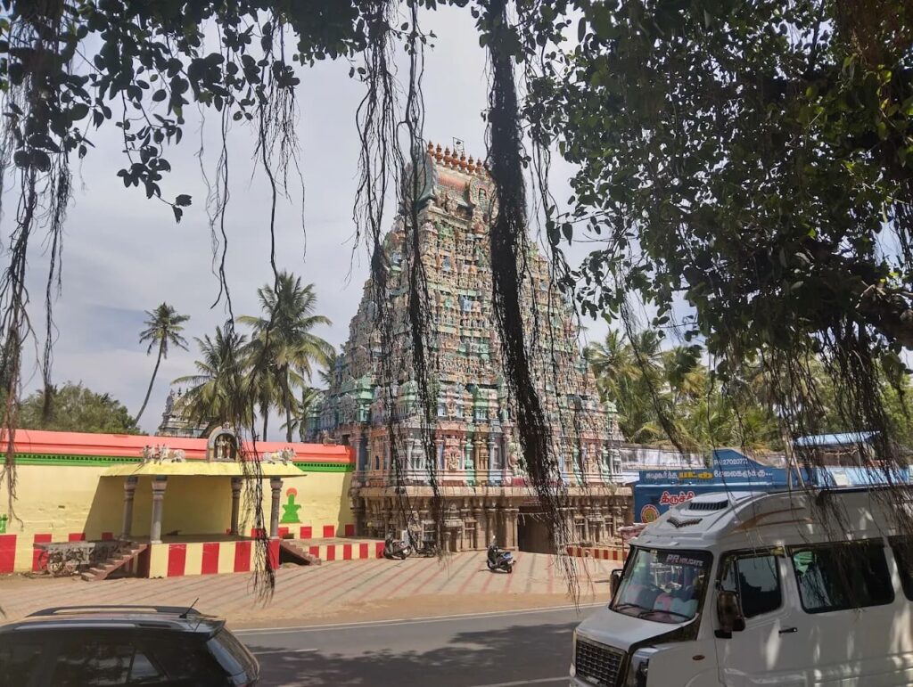 Ancient South Indian temple tower viewed through hanging banyan tree aerial roots.