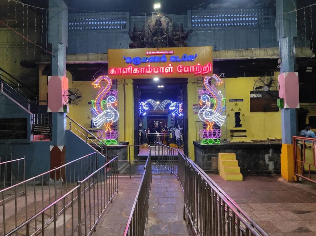 Entrance arch of Kalikambal Temple Chennai featuring illuminated peacock neon lights and queue queue lines