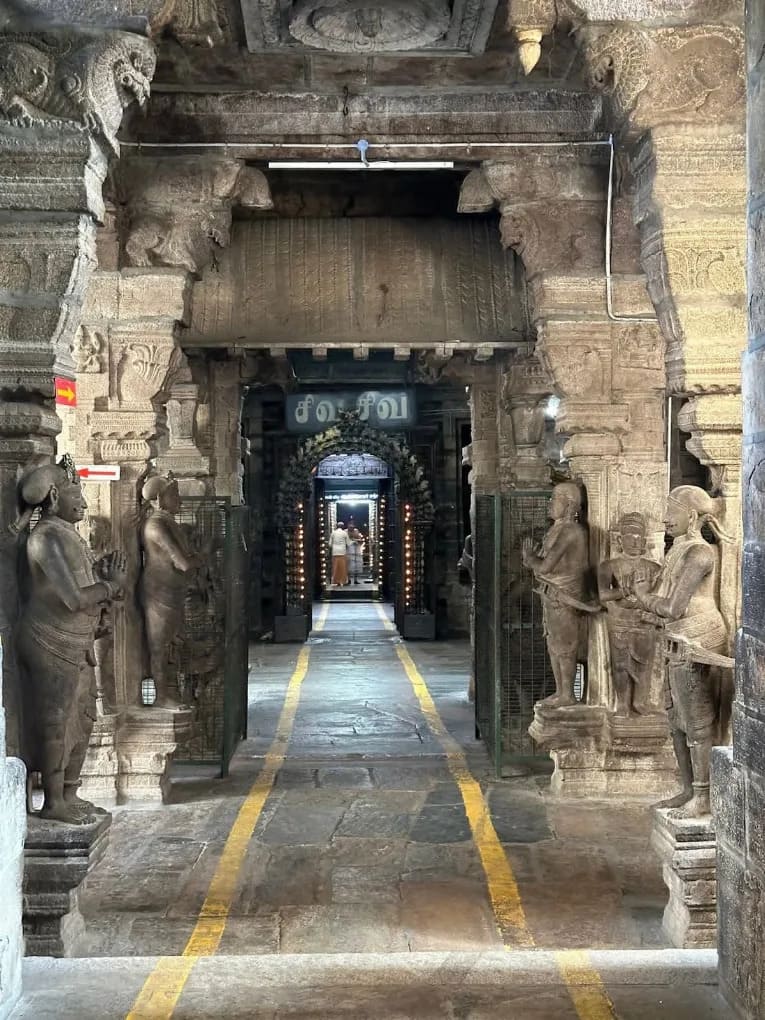 Central passage of Avudaiyarkoil temple showing stone pillars, yellow path markers, and Tamil Siva Siva board Central passage of Avudaiyarkoil temple showing stone pillars, yellow path markers, and Tamil Siva Siva board